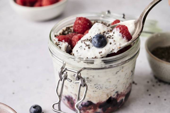 Spoon scooping creamy yogurt chia seed pudding topped with raspberries, blueberries, and chia seeds from a glass jar layered with fruit at the bottom.